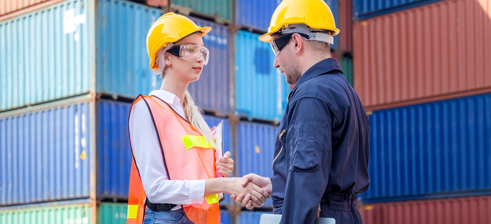 Two workers are shaking hands at a shipping container yard