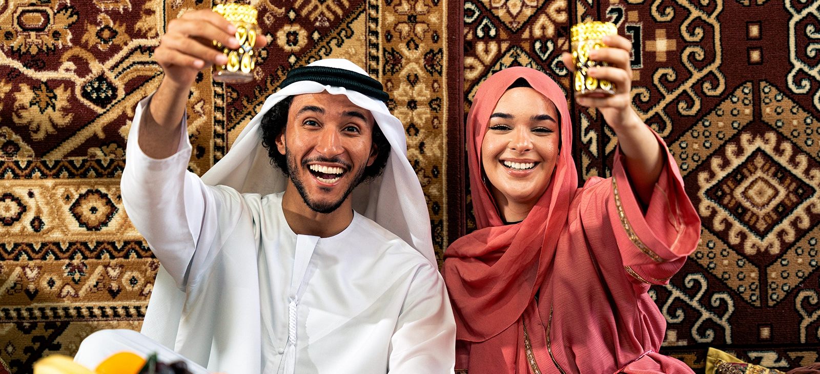 Couple in traditional attire raising cups during a festive celebration.

