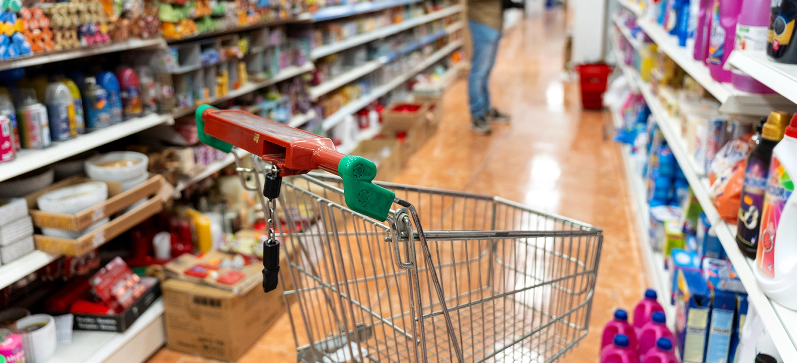 Shopping cart in a supermarket aisle with a customer browsing shelves

